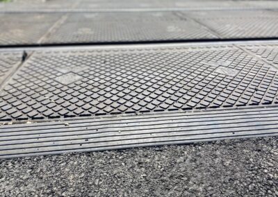 Close-up of a textured metal sheeting with diamond studs creating a tactile surface near the curb over asphalt edge.