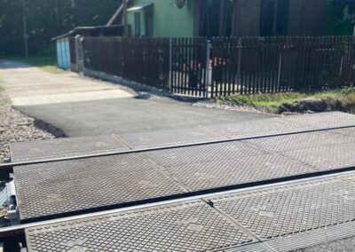 Metal grated pedestrian crossing over train tracks with gravel beneath and a wooden fence in the background