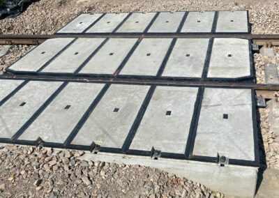 Row of gray precast concrete panels laid on ballast beside a railway track, with small square recesses and black edge strips along the rail line.