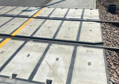 Construction site at a street level crossing with modular concrete panels and rails across the road.