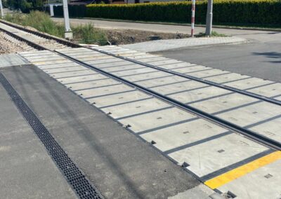 Railroad crossing with metal plates covering tracks and a nearby road in a suburban area under a blue sky.